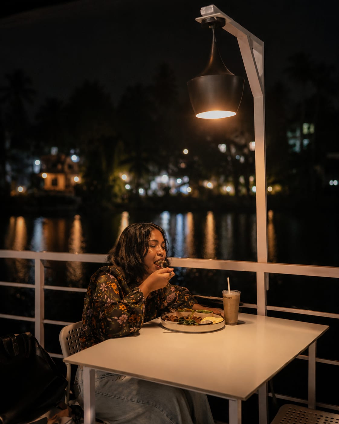 Riverside deck dining at night with lantern glow over dark water